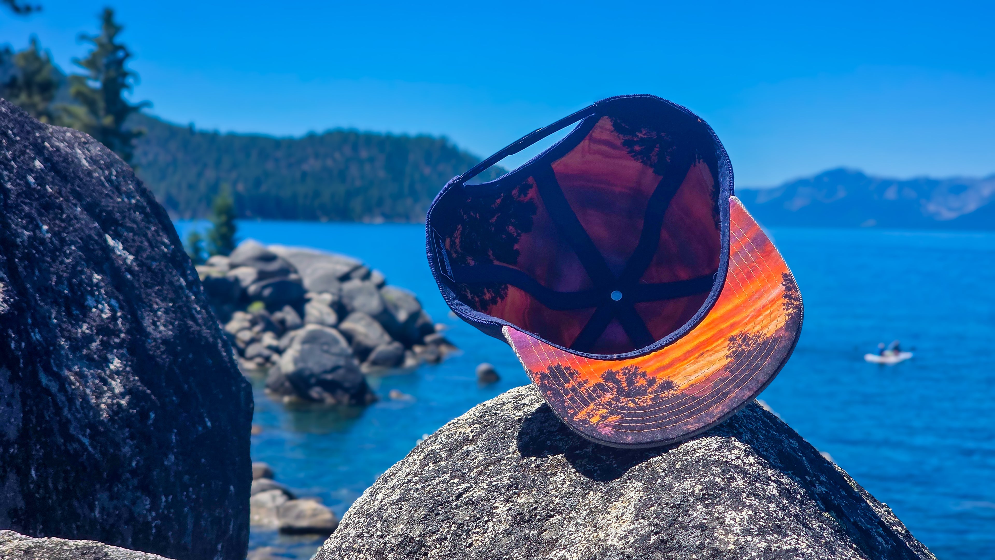 Rooted Sunset Snapback limited edition snapback hat showing colorful sunset underbrim artwork beside Lake Tahoe